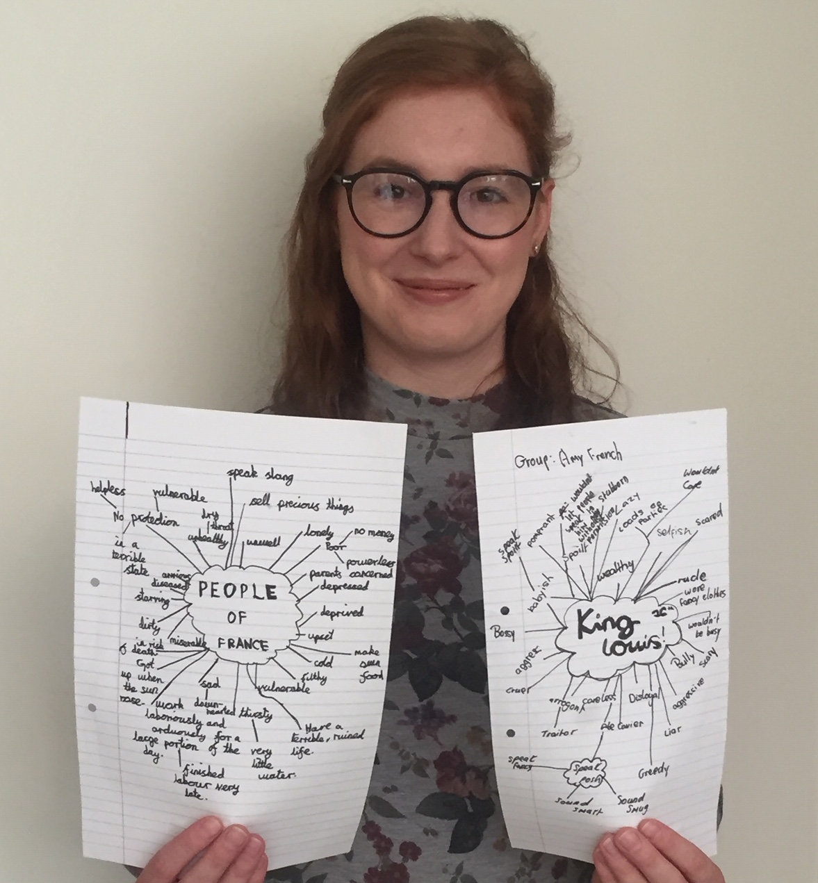 A woman holds two pieces of paper with mind maps on them