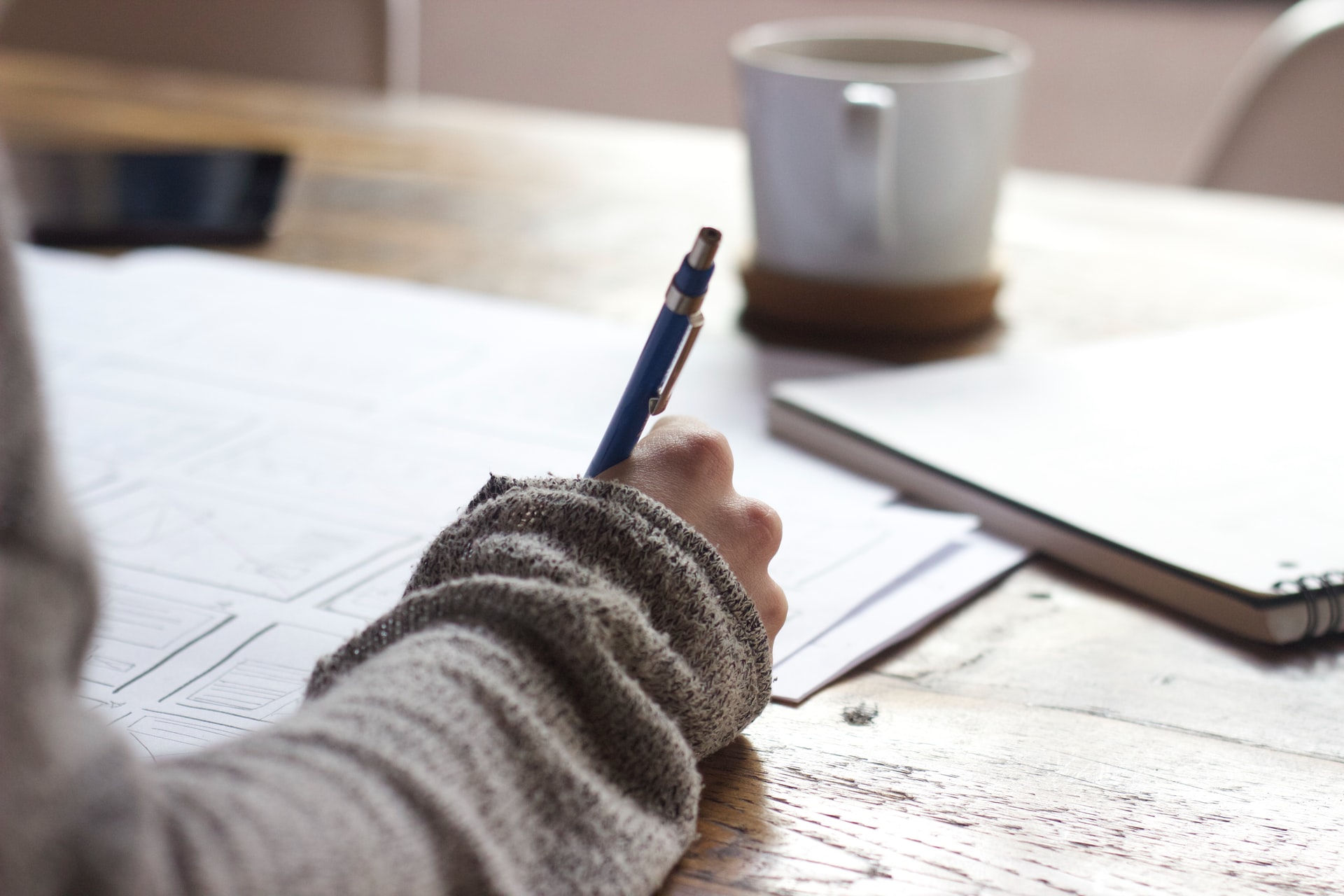 Person sitting at a table writing on paper with a pencil